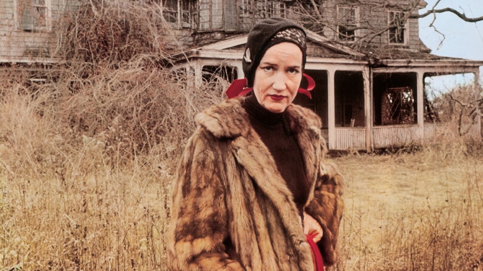Bilde fra filmen Grey Gardens - kvinne i pels foran gammelt hus