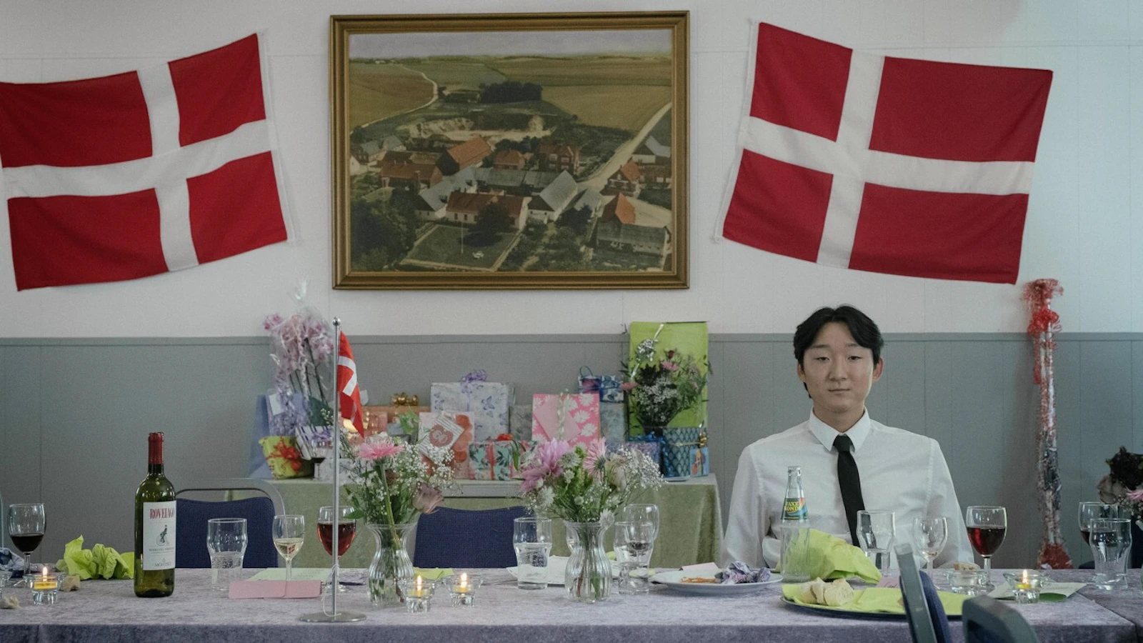 Stillbilde fra filmen Stille liv - mann med asiatisk utseende foran et dansk flagg